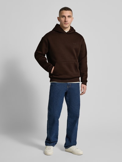 Männermodel trägt Hoodie mit Känguru-Tasche von REVIEW in Dunkelbraun, lockere Passform, Baumwollmischung, Ganzkörperansicht von vorne.
