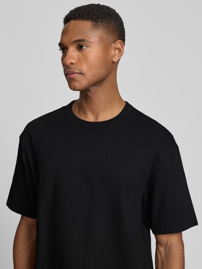 Männermodel trägt Cropped T-Shirt mit Rundhalsausschnitt von GAP, schwarz, reine Baumwolle, glatte Textur, Nahaufnahme Oberkörper.