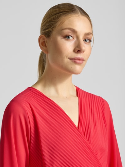 Frauenmodel trägt knielanges Kleid mit Plisseefalten Modell 'Im44sa' von ZABAIONE in Rot, taillierte Wickel-Optik, Nahaufnahme Oberkörper.