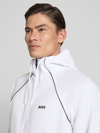 Männermodel trägt Regular Fit Sweatjacke aus Baumwoll-Mix Modell 'SAGGY' von BOSS, unifarben weiß mit schwarzem Saum, Nahaufnahme Oberkörper.