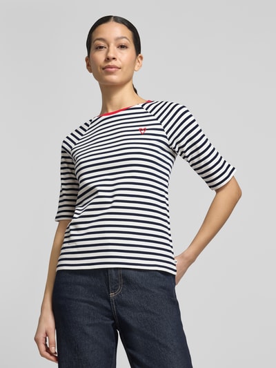 Modelka nosi Shaped Fit T-Shirt aus reiner Baumwolle von Tom Tailor Denim, w paski, krój shaped fit, okrągły dekolt, krótki rękaw, białe i granatowe, aplikacja z sercem, bawełna, prążkowana faktura, widok całej sylwetki z przodu.