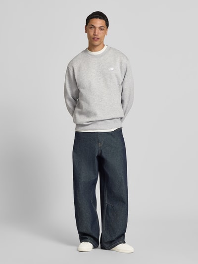 Männermodel trägt Sweatshirt mit Rundhalsausschnitt und Label-Stitching von New Balance aus Baumwoll-Mix in Grau, Relaxed-Fit, Ganzkörperansicht von vorne. Rückenlänge 67 cm, Ärmellänge 63 cm in Größe M.