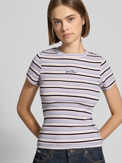 Frauenmodel trägt Slim Fit T-Shirt mit Logo-Stitching von GUESS, weiß mit schwarzen und lila Streifen, Nahaufnahme Oberkörper, elastischer Baumwoll-Mix.