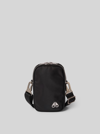 Produktfoto, Crossbody-Bag mit Logo-Detail von Moose Knuckles aus schwarzem Material, silberfarbener Zweiwege-Reißverschluss, Hauptfach mit Reißverschluss, abnehmbarer Tragehenkel, verstellbarer Trageriemen, Maße ca. 11 cm Breite, 18 cm Länge, 4 cm Tiefe, glatte Textur.