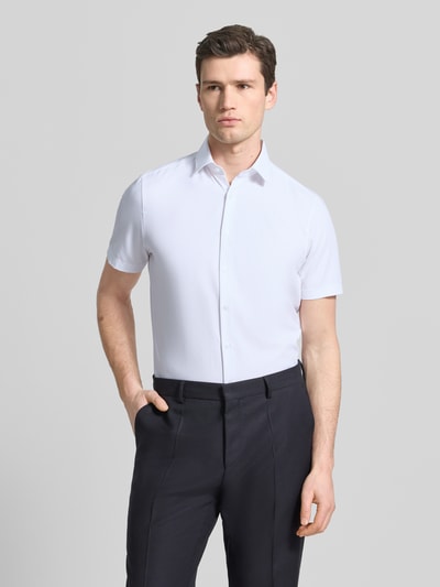 Męski model prezentuje Slim Fit Business-Hemd in kurzärmligem Design Modell 'Modern' von OLYMP Level Five, biały kolor, prosty krój, bawełniano-elastyczny materiał, kołnierzyk Kent, zapięcie na guziki, krótki rękaw, długość pleców w rozmiarze 40: 79 cm, szerokość w rozmiarze 40: 43 cm, długość rękawa w rozmiarze 40: 24 cm, krój slim fit, zdjęcie całej sylwetki od przodu.
