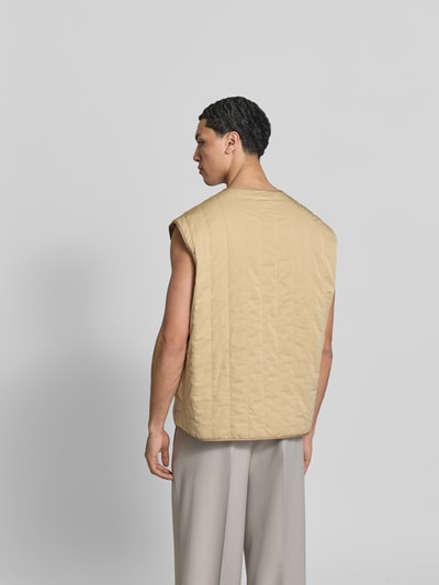 Männermodel trägt Relaxed Fit Weste in Stepp-Optik von MM6 Maison Margiela in Beige mit Eingrifftaschen, Ganzkörperansicht Rückansicht.