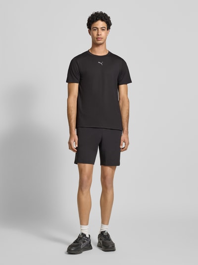 Männermodel trägt Regular Fit T-Shirt mit Rundhalsausschnitt von PUMA PERFORMANCE aus Baumwoll-Viskose-Mix, Logo-Print, Schwarz, Ganzkörperansicht von vorne.