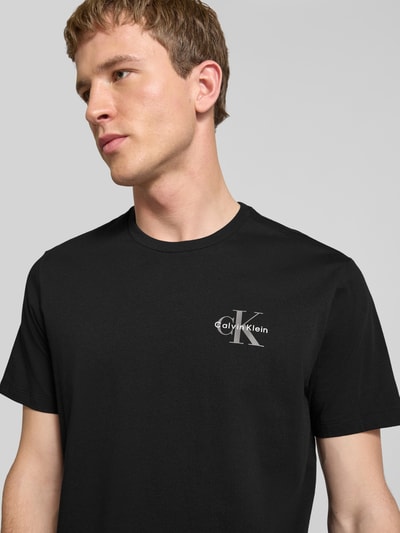Männermodel trägt T-Shirt mit Rundhalsausschnitt und Logo von Calvin Klein Jeans aus reiner Baumwolle, Regular-Fit, Nahaufnahme Oberkörper.