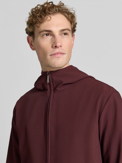Männermodel trägt Jacke mit Kapuze und Zweiwege-Reißverschluss von Emporio Armani in Bordeaux, Material-Mix mit Stretch-Anteil, Regular-Fit, Nahaufnahme Oberkörper.