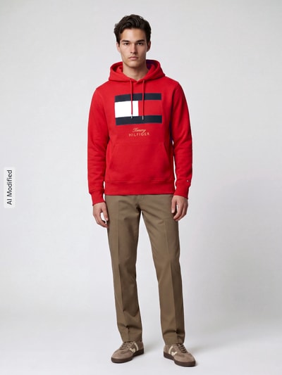 Männermodel trägt Hoodie mit Logo-Print von Tommy Hilfiger in Rot, reine Baumwolle, Kängurutasche, Ganzkörperansicht von vorne, KI-modifiziertes Bild.