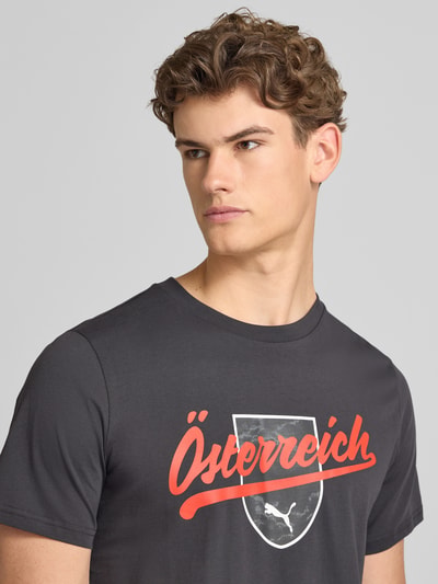 Männermodel trägt T-Shirt mit Print und Rundhalsausschnitt von PUMA PERFORMANCE, Reine Baumwolle, Regular-Fit, Print in Rot, Nahaufnahme Oberkörper.