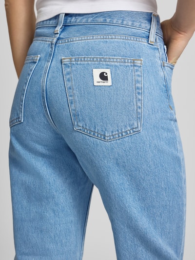 Kobieta nosi Straight Leg Jeans im 5-Pocket-Design Modell 'Noxon' od Carhartt Work In Progress, wykonane z czystej woskowanej bawełny, krój straight fit; detal produktu: guziki i zamek, szerokość w rozmiarze 27: 37 cm, długość nogawki wewnętrznej: 81 cm, jasnoniebieski denim, tekstura gładka; detaliczne ujęcie tylnej kieszeni, zbliżenie na górną część nogi z tyłu.