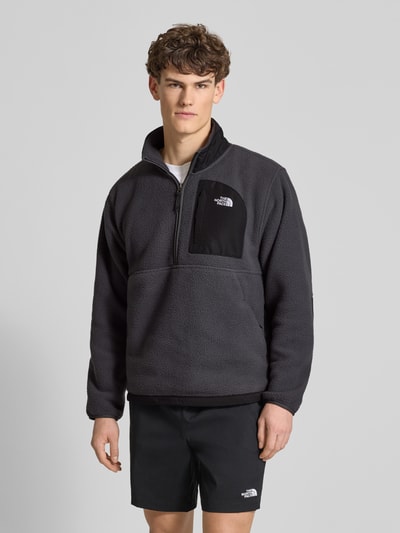 Männermodel trägt Fleecepullover mit Napoleontasche Modell 'YUMIORI' von The North Face in Schwarz, glatte Struktur, Ganzkörperansicht von vorne.