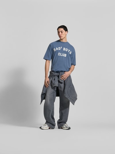 Männermodel trägt Loose Fit T-Shirt mit Rundhalsausschnitt von Dsquared2 in Blau mit Statement-Print und Used-Look, Ganzkörperansicht von vorne.