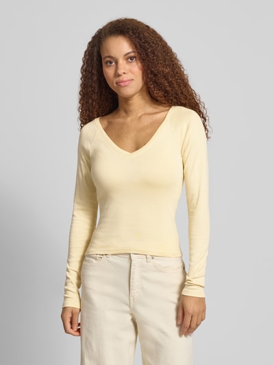 Modelka kobieca nosi Slim Fit Longsleeve mit V-Ausschnitt od Gina Tricot, bawełniany elastyczny materiał, długi rękaw, krój slim fit, kremowy kolor, długość tyłu w rozmiarze S: 48 cm, widok na cały korpus z przodu.