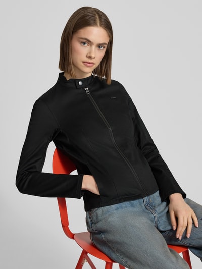 Modelka kobieta ma na sobie Slim Fit Bikerjacke mit Label-Detail Modell 'Lynn' od G-Star Raw, czarny bawełniano-elastanowy krój slim fit, stebnowany stojący kołnierz, zamek błyskawiczny, subtelne logo, gładka tekstura, długość tyłu w rozmiarze S: 53 cm, szerokość ramion w rozmiarze S: 38 cm, szerokość w rozmiarze S: 41 cm, długość rękawa w rozmiarze S: 61 cm, całe ciało widoczne z przodu