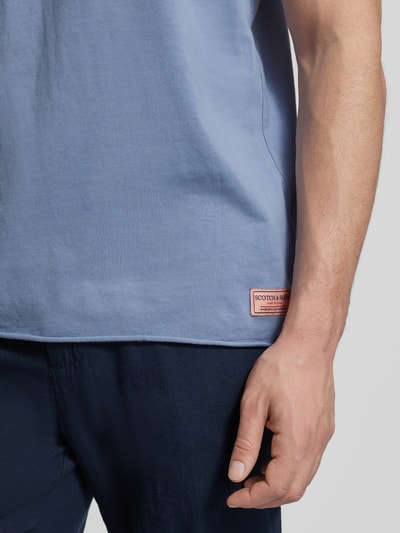Männermodel trägt T-Shirt mit Rundhalsausschnitt und Label-Detail von Scotch & Soda, Reine Baumwolle, Regular-Fit, Rollsaum, Nahaufnahme Oberkörper.