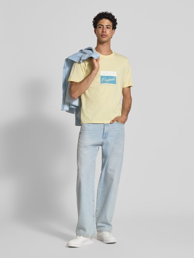 Männermodel trägt T-Shirt mit Statement-Print Modell 'RHYERES' von Jack & Jones in Gelb, Regular Fit, Rundhalsausschnitt, helle Jeans, Ganzkörperansicht von vorne.