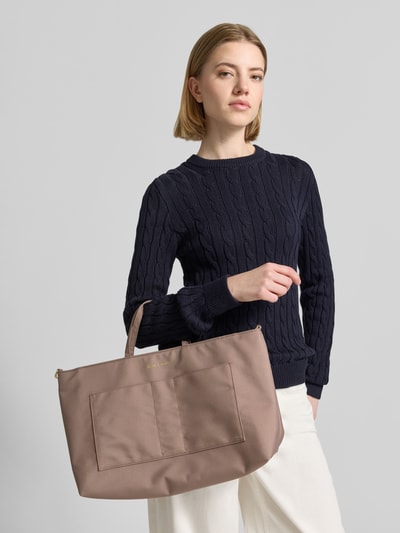 Frauenmodel trägt Handtasche mit Logo-Detail von Hey Marly in Taupe mit schmalen Schulterriemen und Steckfächern, Nahaufnahme Oberkörper.