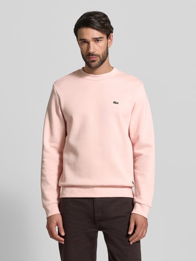 Mannelijk model draagt Classic Fit Sweatshirt uit katoenmix van Lacoste in effen lichtroze met logo-stitching, ronde hals, lange mouwen, geribde boorden, borstdetail, classic fit. Volledige frontale aanzicht van het bovenlichaam.