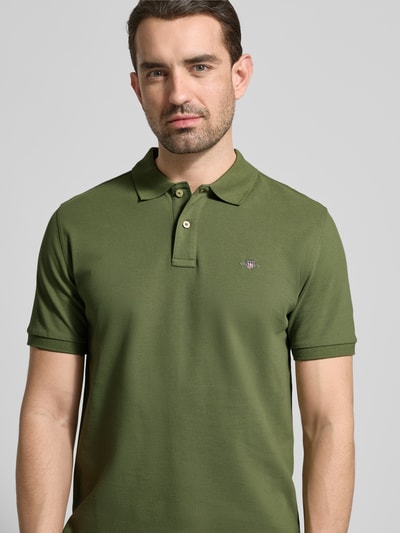 Männermodel trägt Slim Fit Poloshirt mit Logo-Stitching von Gant aus Reine Baumwolle in Olivgrün, Nahaufnahme Oberkörper.