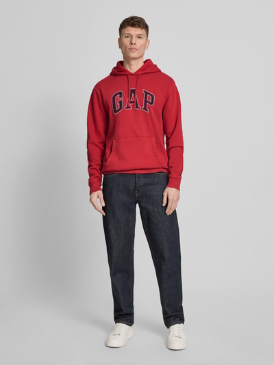 Mannenmodel draagt Hoodie mit Logo und Känguru-Tasche van GAP, katoenmix, regular fit, rood, logo, kangoeroezak, volledige lichaamsvoorzijde.