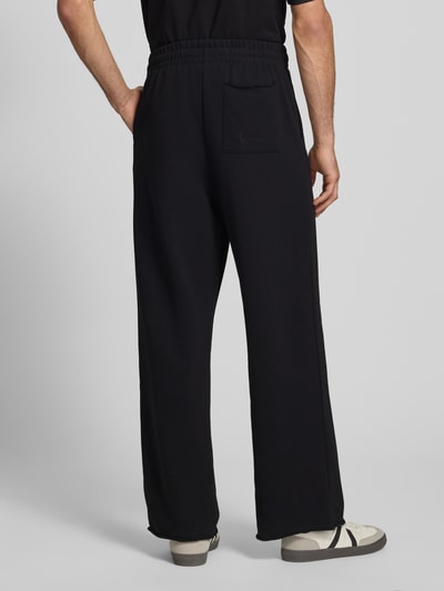 Männermodel trägt Straight Fit Sweatpants mit Gesäßtasche von KARL KANI in Schwarz, Baumwoll-Mix, elastischer Bund, Ganzkörperansicht Rückansicht.