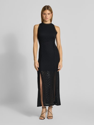 Modelka prezentuje długą sukienkę z koronki i rozporkiem Maxikleid mit Spitze und Gehschlitz Modell 'NEW LIZA' od Guess, czarny, dopasowany krój, półprzezroczysty materiał, okrągły dekolt, wycięcie na plecach, halka pod sukienkę; mieszanka materiałów z dodatkiem streczu; szerokość w rozmiarze S: 35 cm, długość tyłu: 143 cm, widok całej sylwetki z przodu.