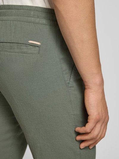 Mężczyzna nosi Hose aus Baumwoll-Leinen-Mix Modell 'KANE' od Jack & Jones, kolor zielony, tkanina z widoczną strukturą, krój regular fit, elastyczny pas, szerokość w rozmiarze M: 41 cm, długość nogawki od wewnątrz w rozmiarze M: 81 cm, zbliżenie na tył.