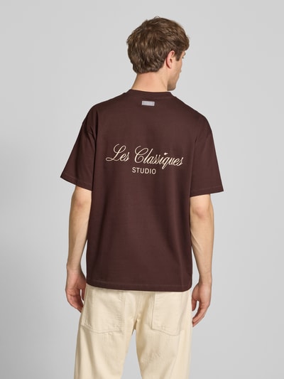 Männermodel trägt Loose Fit T-Shirt aus reiner Baumwolle Modell 'LES CLASSIQUES' von Only & Sons in Braun mit beigem Schriftzug-Print, Jersey-Textur, Ganzkörperansicht Rückansicht.