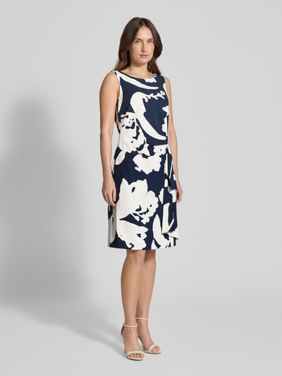 Frauenmodel trägt Knielanges Cocktailkleid in Wickel-Optik von Vera Mont, blau-weißer Print, tailliert, Rundhalsausschnitt, Ganzkörperansicht von vorne.