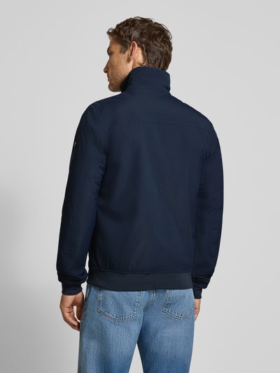 Männermodel trägt Regular Fit Jacke mit Stehkragen Modell 'Alvin' von Didriksons in Dunkelblau, strukturierter Stoff, Ganzkörperansicht Rückansicht. Rückseite zeigt elastische Abschlüsse, Reißverschluss und lockere Schulterpartie, Rückenlänge 68 cm, Schulterbreite 44 cm, Brustweite 56 cm, Ärmellänge 69 cm.