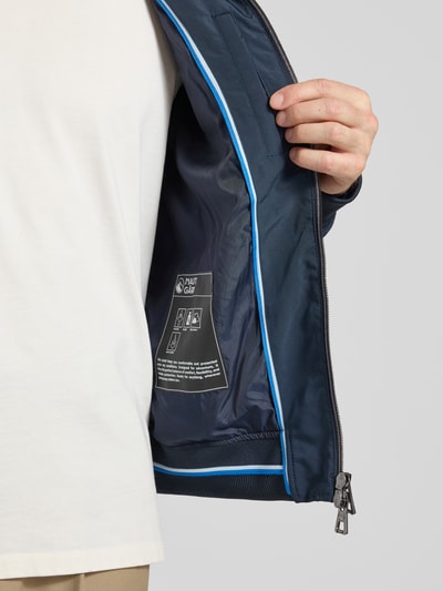 Männermodel trägt Regular Fit Jacke mit Kapuze van NAUTGÅRD in marineblauw met lichtblauwe accenten, detailopname binnenkant. Stehkragen, regular fit, capuchon, steekzakken met rits, tweewegrits, elastische boorden. Ruglengte bij maat M: 67 cm, schouderbreedte: 48 cm, borstwijdte: 60 cm, mouwlengte: 67 cm.