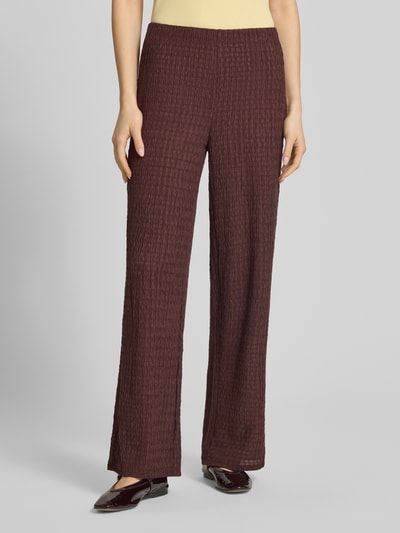 Frauenmodel trägt Straight Leg Hose in Strukturoptik Modell 'ILSE' von Only, Optik: Unifarben, Passform: Straight Leg, Materialverarbeitung: Crinkle, Bundabschluss: elastisch, Mid Waist, rotbraune Farbe, strukturierte Textur, Ganzkörperansicht von vorne.