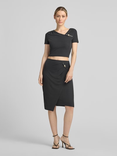Frauenmodel trägt Slim Fit Rock in Knielänge Modell 'Karole' von GUESS, Elastischer-Material-Mix, schwarze Farbe, Dornschließe, Ganzkörperansicht von vorne.