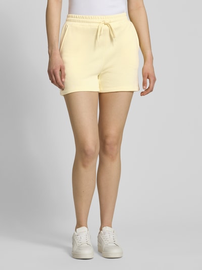 Kobiece model nosi Regular Fit Sweatshorts aus Baumwoll-Mix Modell 'CHILLI' od Pieces, efekt: jednolity kolor, krój regular fit, ściągacz z tunel, wpuszczane kieszenie, wykończenie materiału: dzianina dresowa, materiał: mieszanka bawełny, jasny żółty, gładka tekstura, widok całej sylwetki z przodu.