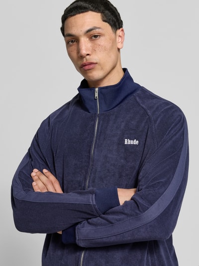 Männermodel trägt Oversized Sweatjacke aus Baumwolle von RHUDE, Frottee, Zweiwege-Reißverschluss, elastische Abschlüsse, Nahaufnahme Oberkörper.