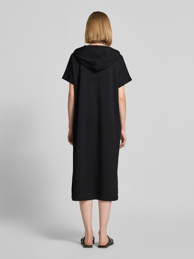 Frauenmodel trägt Sweatkleid mit Kapuze von Soyaconcept in Schwarz, Material-Mix mit Modal-Anteil, Gerader-Schnitt, Midikleid, Label-Print, Ganzkörperansicht Rückansicht.