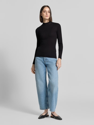 Vrouwenmodel draagt Slim Fit gebreide pullover uit puur katoen model 'ALAANIA' van Armedangels, look: effen, langemouw, hooggesloten, labelpatch, gestikt logo, materiaalverwerking: knitwear, kleur zwart, ganzecorpsaanzicht van voren.