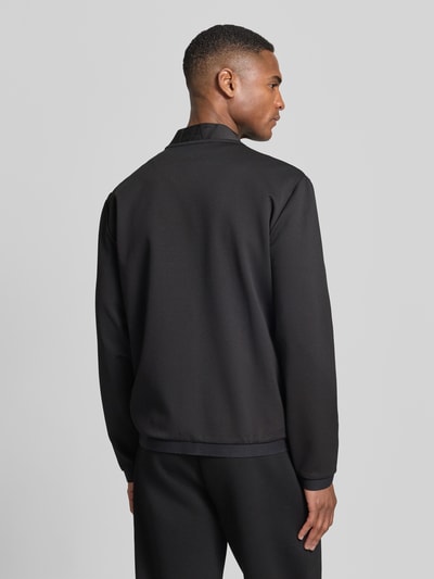 Männermodel trägt Bluza rozpinana mit zamek błyskawiczny dwustronny von EA7 Emporio Armani, mieszanka materiałów z dodatkiem wiskozy, krój regular fit, stójka, naszywka z logo, kieszenie zapinane na zamek błyskawiczny, długość tyłu w rozmiarze M 65 cm, długość rękawów 65 cm, widok całej sylwetki z tyłu.