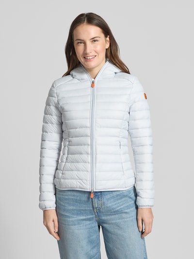 Frauenmodel trägt Slim Fit Steppjacke im Zweiwegereißverschluss Modell 'Daisy' von SAVE THE DUCK in hellblau, gesteppt, mit Kapuze und Reißverschlusstaschen, Ganzkörperansicht von vorne.
