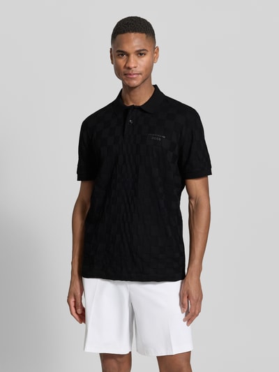 Männermodel trägt Poloshirt aus reiner Baumwolle Modell 'JACQ' von BOSS Green x Porsche in Schwarz mit Strukturmuster, Ganzkörperansicht von vorne.