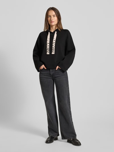 Frauenmodel trägt Oversized Sweatshirt mit Tunnelzug von Marc Cain aus schwarzem Baumwoll-Mix mit Stretch-Anteil, Stehkragen, Ganzkörperansicht von vorne.