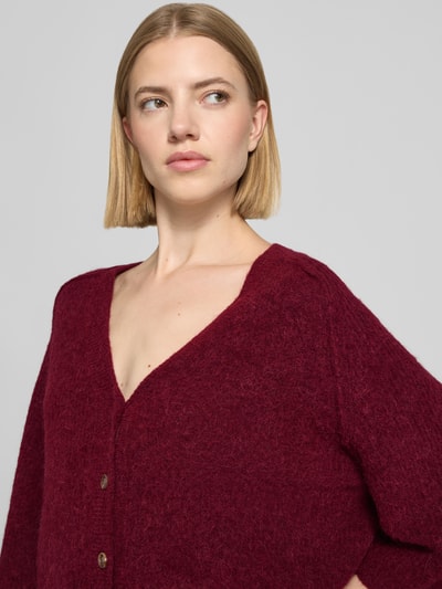 Frauenmodel trägt Strickjacke aus Alpaka-Mix mit Leinen-Anteil Modell 'Thora' von MOS MOSH in Burgunderrot, Nahaufnahme Oberkörper. Gerade Passform, V-Ausschnitt, Knopfleiste sowie 3/4-Arm, weiche melierte Textur.