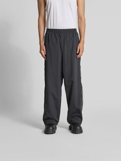 Männermodel trägt Sweatpants mit elastischem Bund von VETEMENTS in Schwarz, Relaxed-Fit, Eingrifftaschen, Beinabschlüsse mit Tunnelzug, Wide Leg, Ganzkörperansicht von vorne.