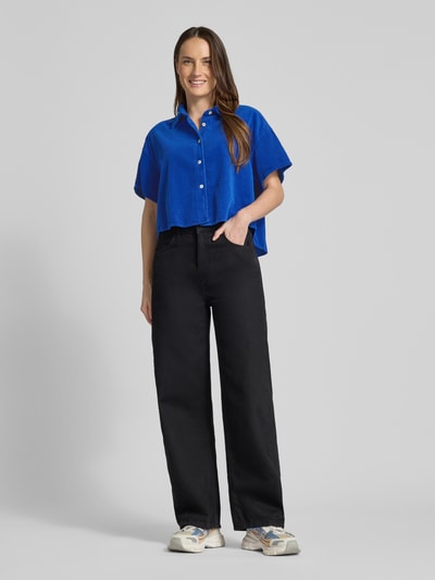 Modelka nosi Cropped Hemdbluse mit Knopfleiste Modell 'PADOW' od American Vintage w kolorze niebieskim, luźny krój, bawełna, półrękaw, widok całej sylwetki z przodu.