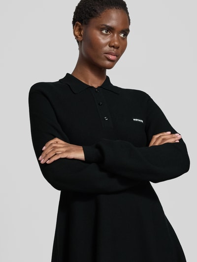 Frauenmodel trägt schwarzes Strickkleid mit Label-Detail von ROTATE im Modal-Woll-Mix, Hemdblusenkragen, taillierter Schnitt, Nahaufnahme Oberkörper.