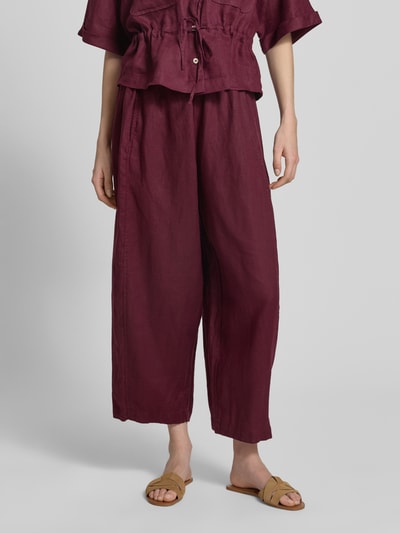 Frauenmodel trägt Leinenhose in verkürzter Passform mit elastischem Bund von Christian Berg Woman in Dunkelrot, Wide-Leg, Tunnelzug, Reines Leinen, Innenbeinlänge 64 cm, Ganzkörperansicht von vorne.