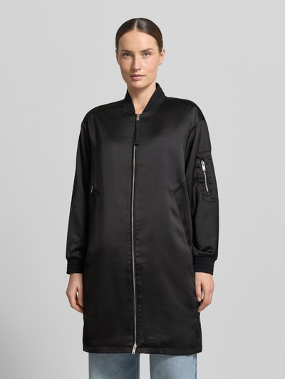 Kobiece modelka nosi kurtkę Jacke mit Zweiwege-Reißverschluss Modell 'TINDRA' od khujo, czarna, mieszanka materiałów z dodatkiem streczu, krój regular fit, stójka, długość tyłu w rozmiarze S 90 cm, szerokość ramion w rozmiarze S 49 cm, szerokość w rozmiarze S 55 cm, długość rękawów w rozmiarze S 54 cm, przód, widok całej sylwetki.