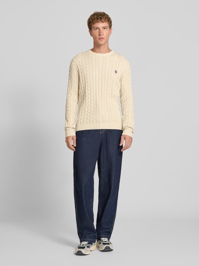Männermodel trägt Slim Fit Strickpullover reine Baumwolle von REVIEW in Creme mit Zopfmuster und Logo Stickerei, Ganzkörperansicht von vorne. Rückenlänge 73 cm, Ärmellänge 70 cm, gerippte Bündchen.
